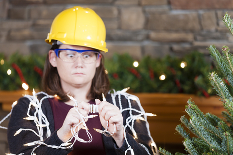 lady in a hardhat plugging in lights next to a christmas tree