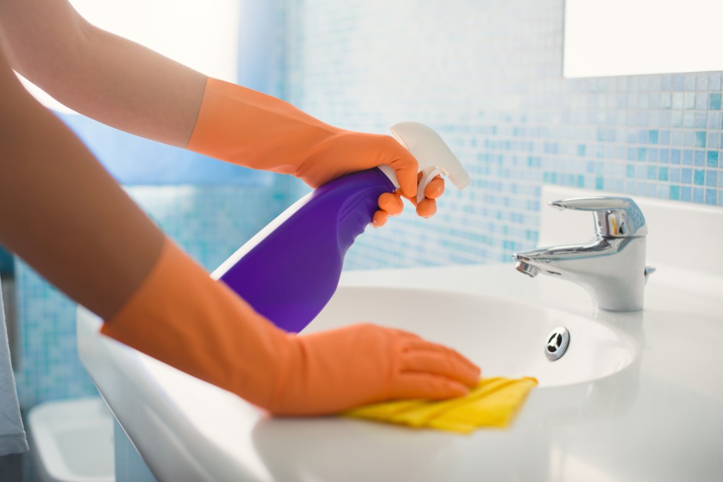 cleaning a bathroom sink with a purple spray-bottle and yellow cloth