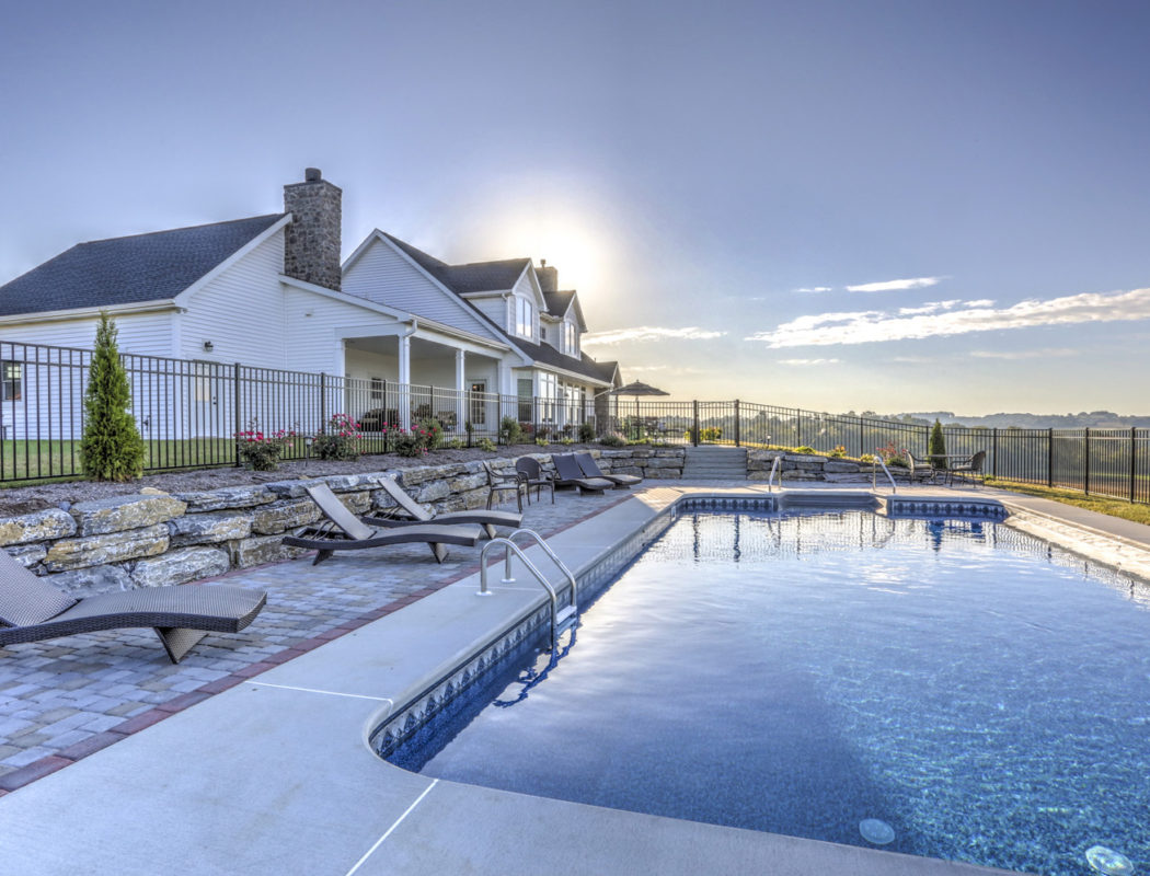 fenced in in-ground pool area with lounge chairs