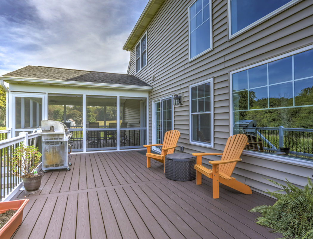 a deck with 2 orange chairs and grill