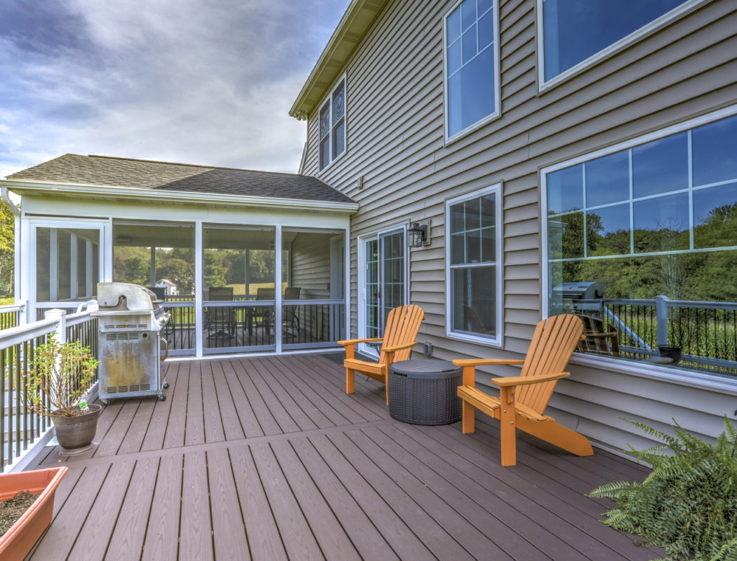 a deck with 2 orange chairs and grill