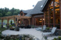 back of a log home with a wood shade structure and hardscaped patio