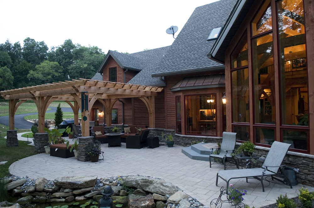 back of a log home with a wood shade structure and hardscaped patio