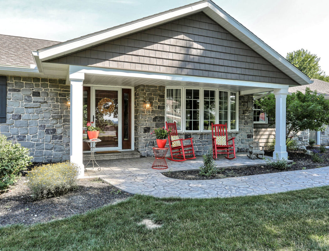 a stone walkway leading up to a nice porch with 2 red rocking chairs
