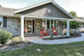 a stone walkway leading up to a nice porch with 2 red rocking chairs